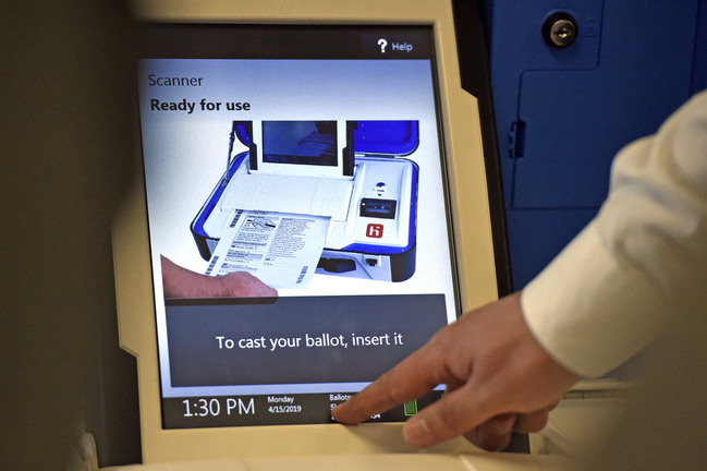 White touch screen reads "Scanner. Ready for use. To cast your ballot, insert it" with a timestamp of 1:30 pm. White hand touches bottom of screen.