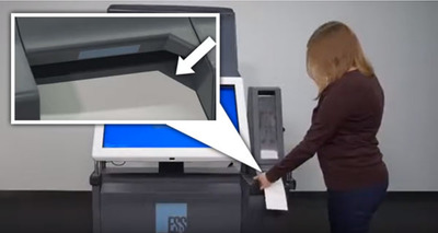Voter with red hair and brown shirt puts white ballot card into ExpressVote XL voting machine