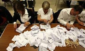 paper ballots on a table with three poll workers sorting them