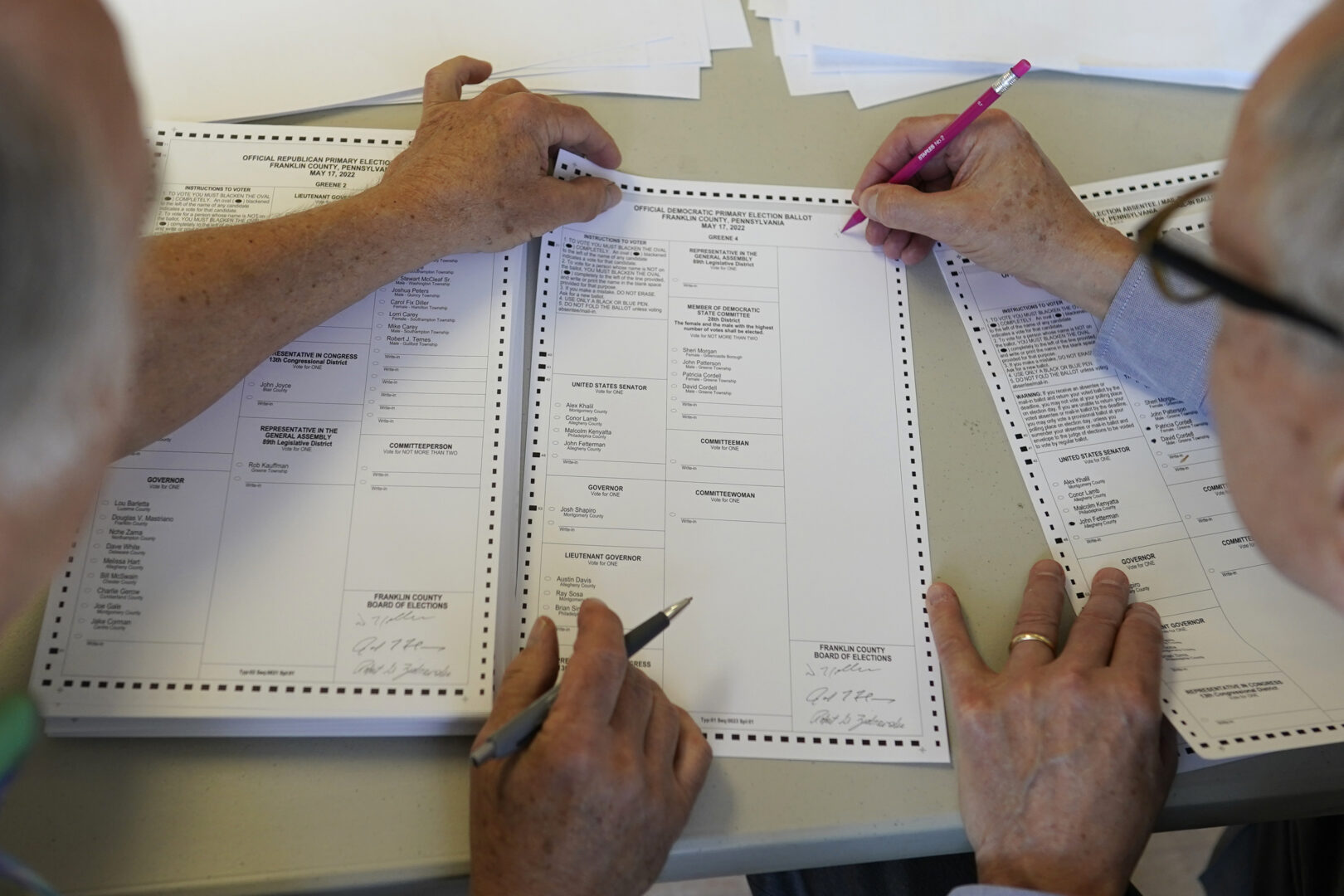 Two workers holding pencils handle a ballot