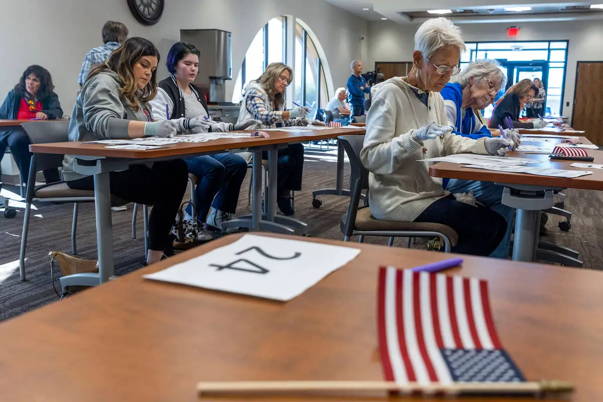 Volunteers seated at tables hand counting ballots in Nye County at the Valley Conference Center. American flag on desk in forefront